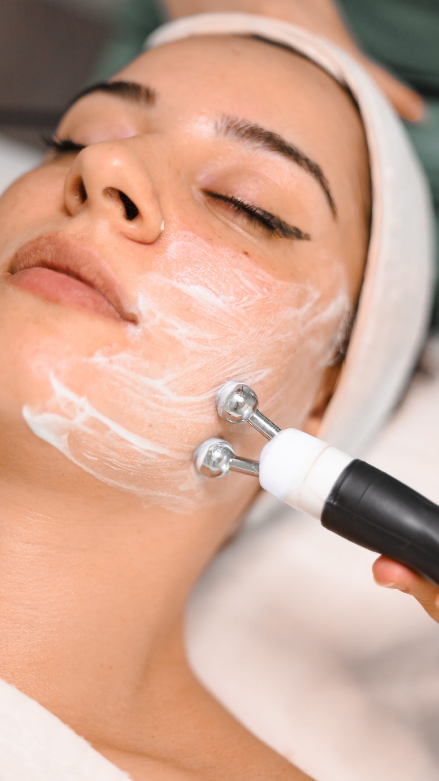 Primer plano de una mujer recibiendo un tratamiento facial con un masajeador y crema facial